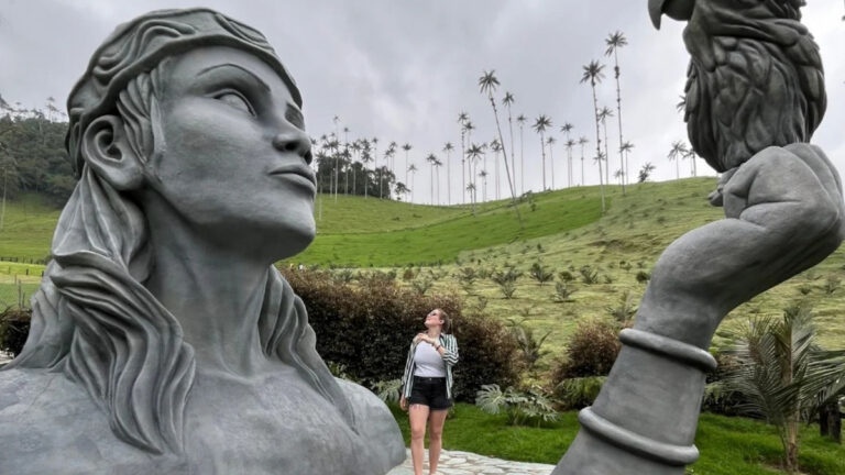 A traveler at a sculpture with the wax palms of the Cocora Valley behind