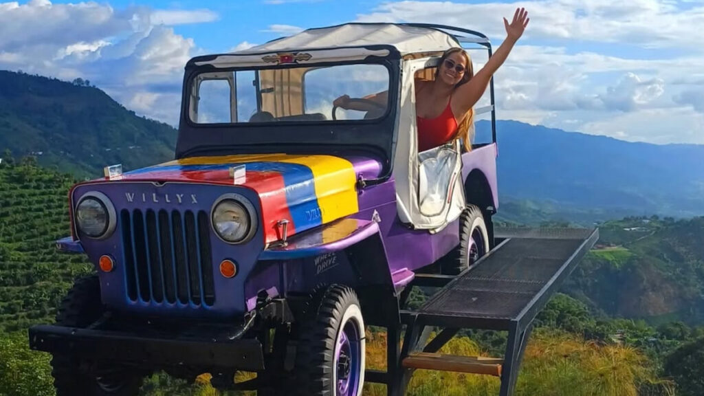 Traveler waving from a Willys jeep at a mountain viewpoint in Buenavista, Quindío, Colombia.