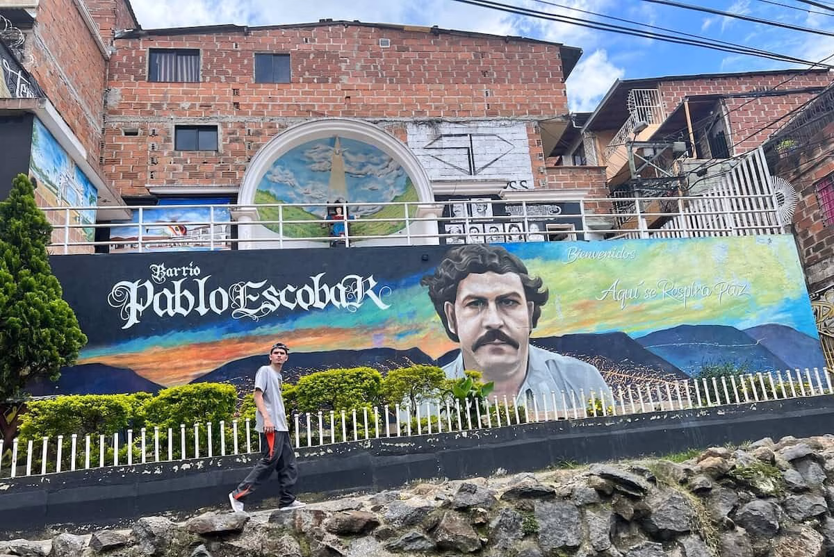Visitor walking past a mural in Barrio Pablo Escobar, Medellín, Colombia.