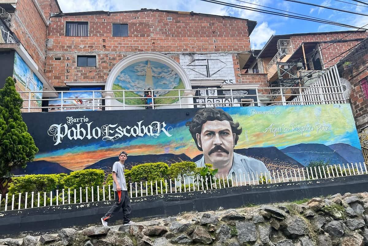 Visitor walking past a mural in Barrio Pablo Escobar, Medellín, Colombia.