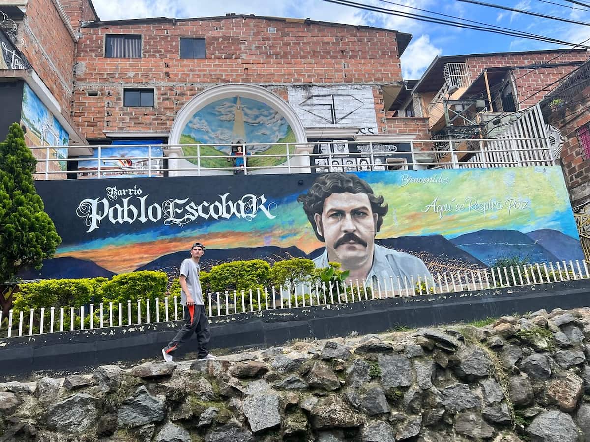 Visitor walking past a mural in Barrio Pablo Escobar, Medellín, Colombia.