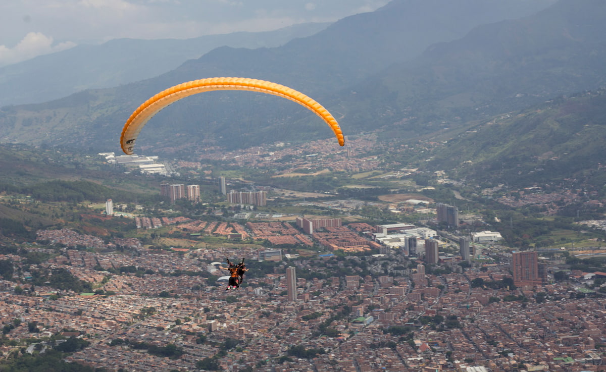 Orange paraglider flying over the Aburrá Valley during paragliding in Medellín, Colombia