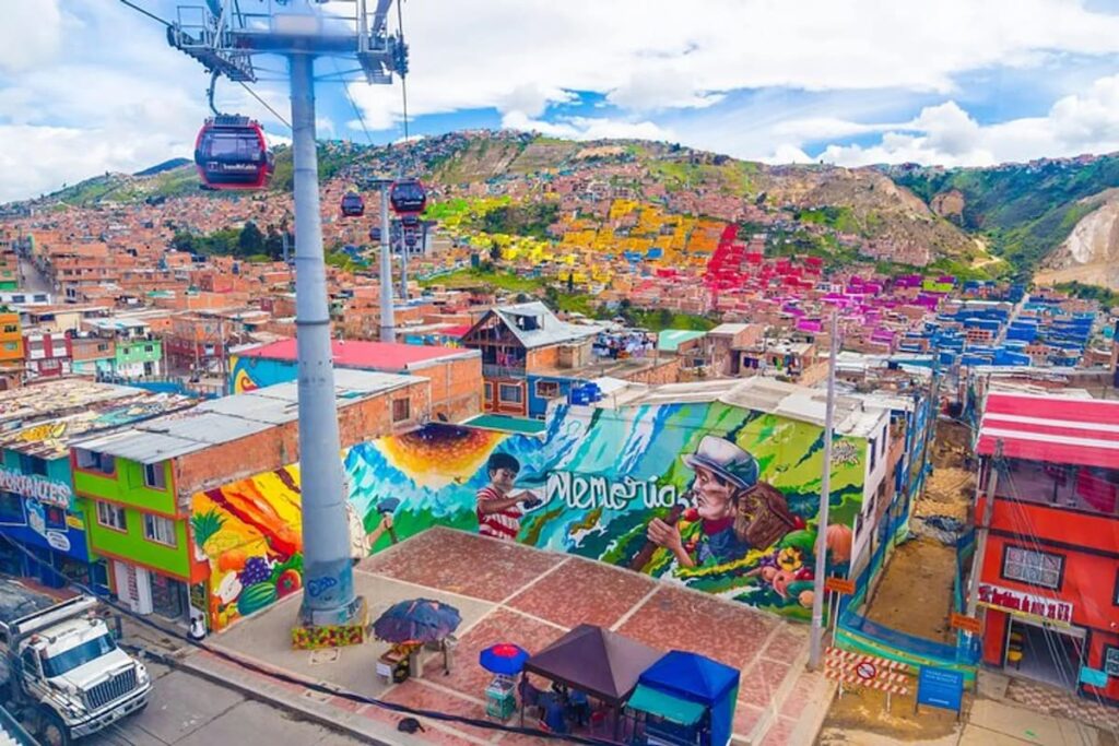Cable cars passing over colorful murals on the El Paraíso Favela Tour in Ciudad Bolívar, Bogotá, Colombia.