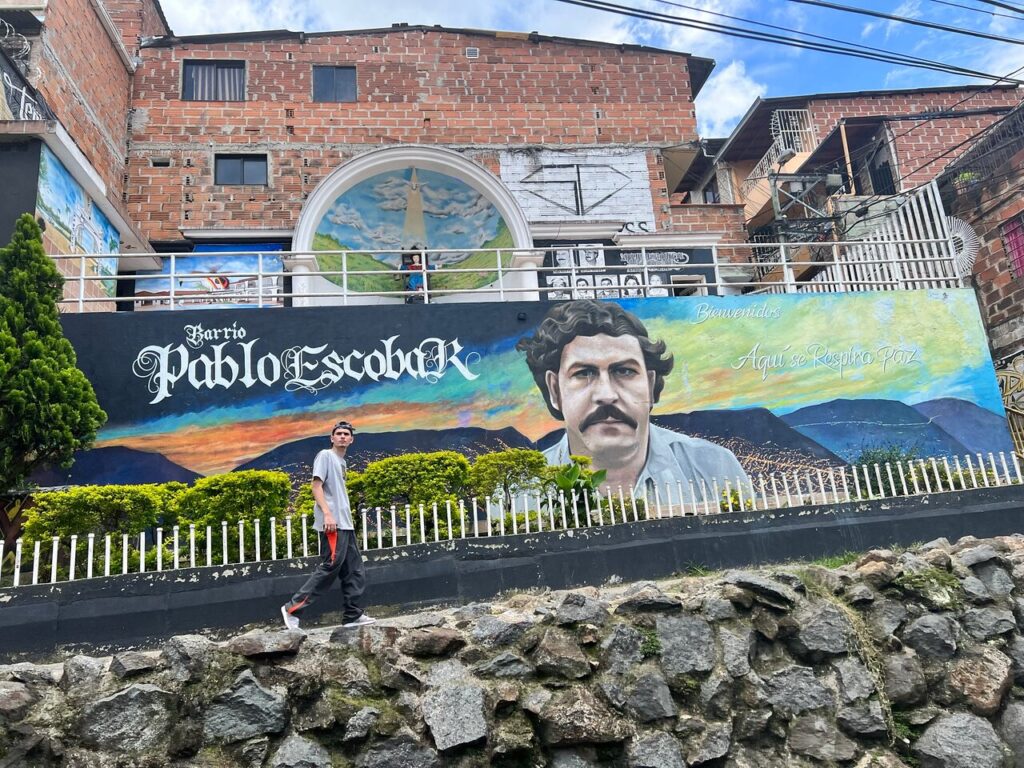 Visitor walking past a mural in Barrio Pablo Escobar, Medellín, Colombia.
