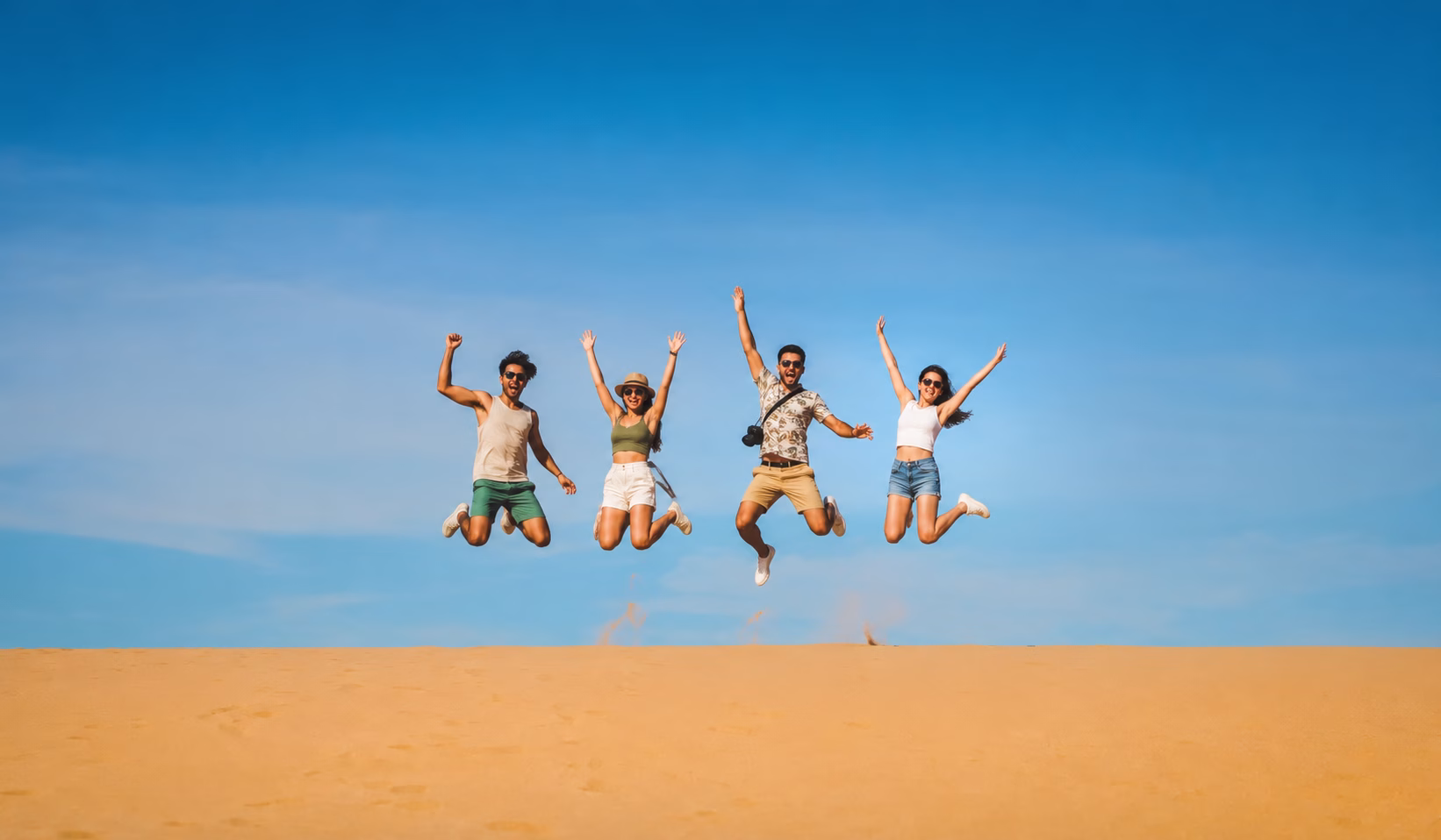 Travelers jumping on golden sand dunes under a clear blue sky on the 3 day tour La Guajira.