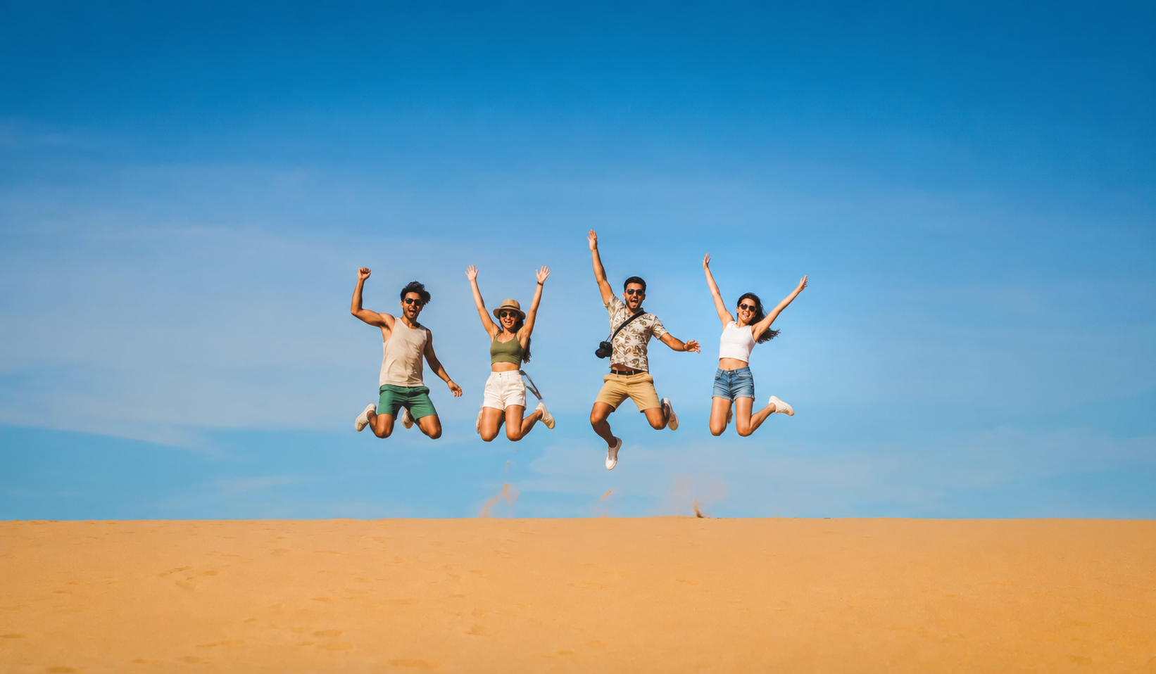 Travelers jumping on golden sand dunes under a clear blue sky on the 3 day tour La Guajira.