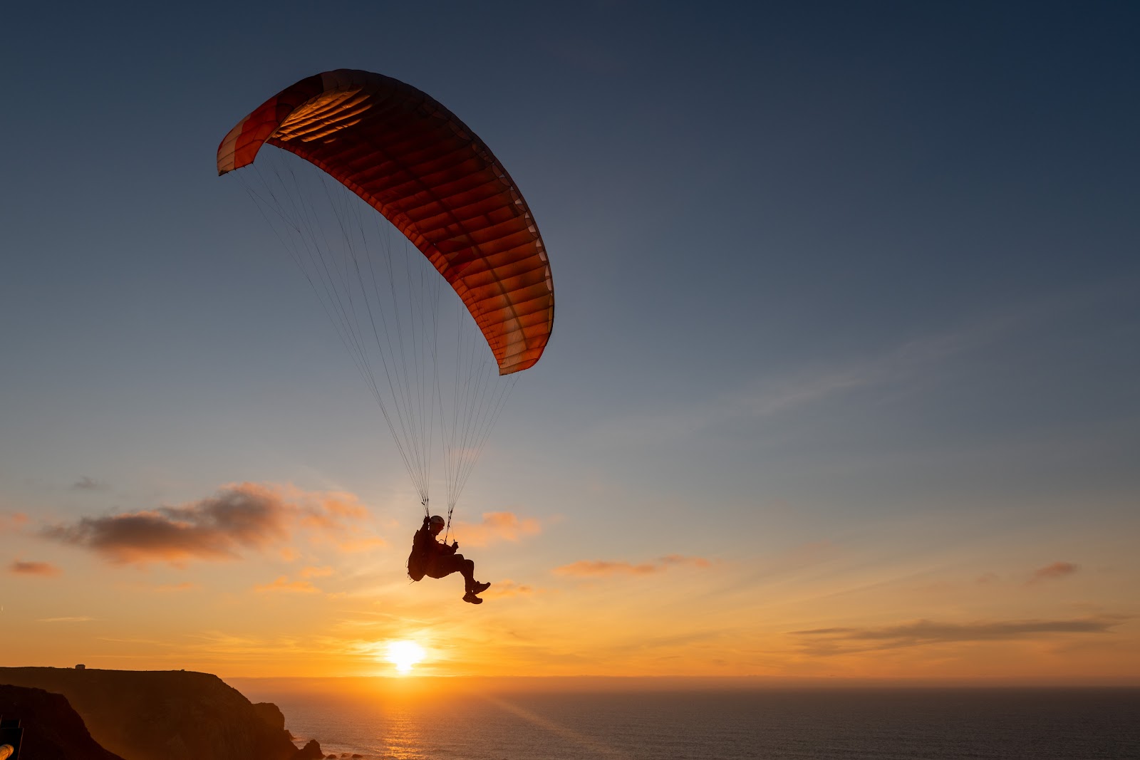 Silhouette of a paraglider soaring above the ocean at sunset, capturing the thrill of paragliding Chicamocha Canyon.