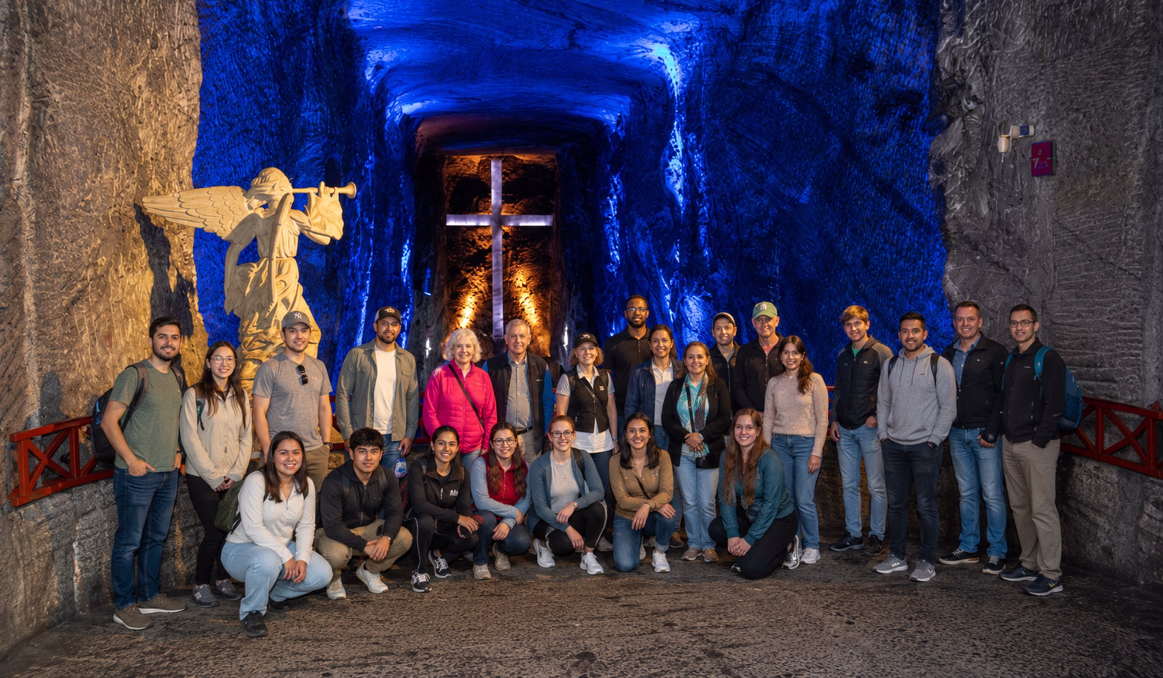 Foto de grupo dentro de la Catedral de Sal durante un tour de 2 días Zipaquirá Villa de Leyva, con túneles iluminados de azul, una cruz brillante y esculturas talladas en sal al fondo.