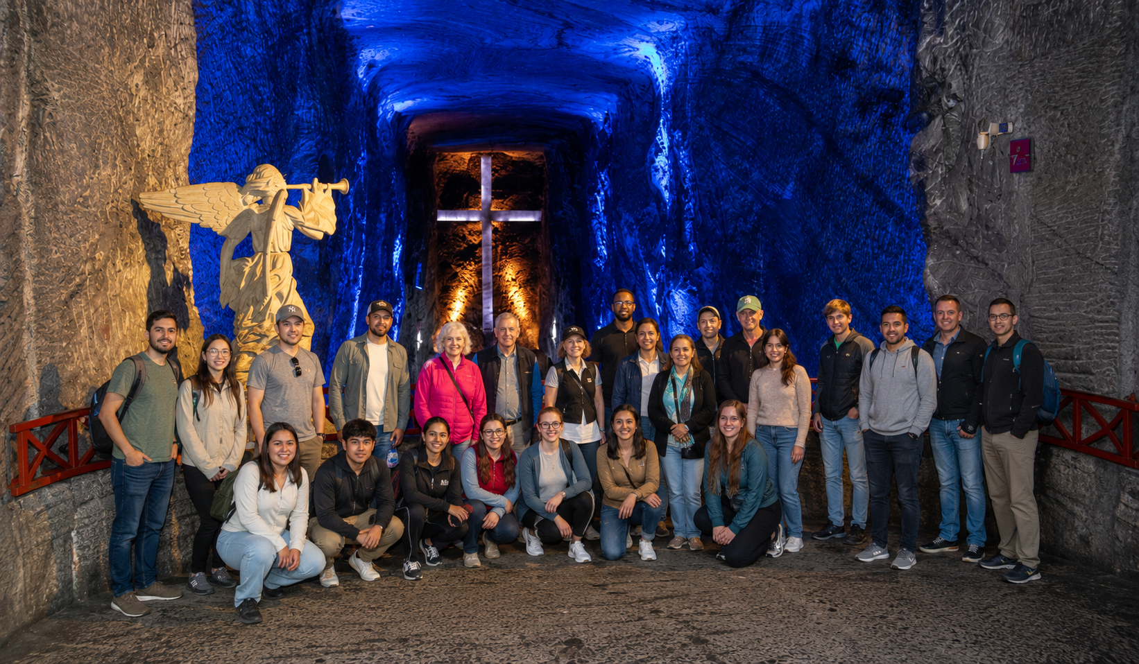 Group photo inside the Salt Cathedral during a 2 day tour Zipaquirá Villa de Leyva, with blue-lit tunnels, a glowing cross, and carved salt sculptures in the background.