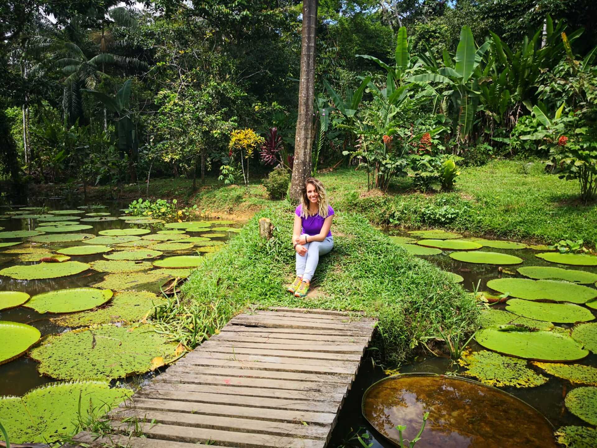 Traveler sitting beside giant water lilies in a tropical garden on an Amazon Three Borders Tour Colombia.