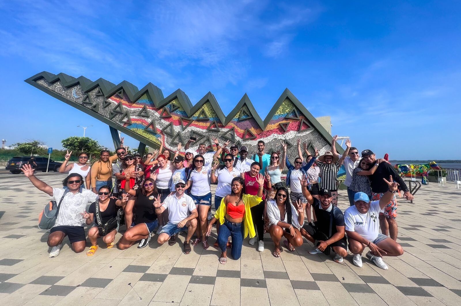 Group of visitors smiling by a modern riverside sculpture on a sunny Barranquilla City Tour..