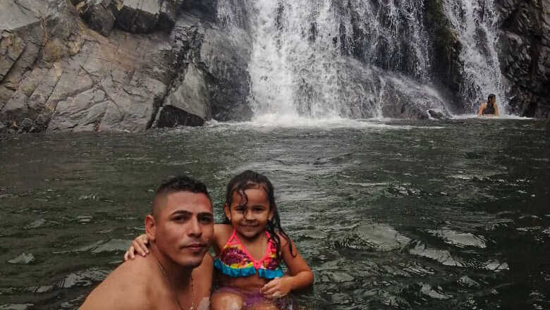Padre e hija nadando bajo una cascada en la piscina natural de Palomino.