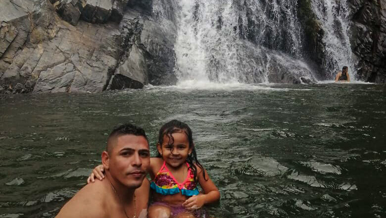 Father and daughter enjoying a swim beneath a waterfall at the Natural pool Palomino.