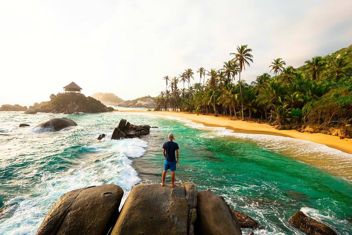 Visitor standing on coastal rocks with a tropical beach and ocean views on a Tayrona Park Tour.