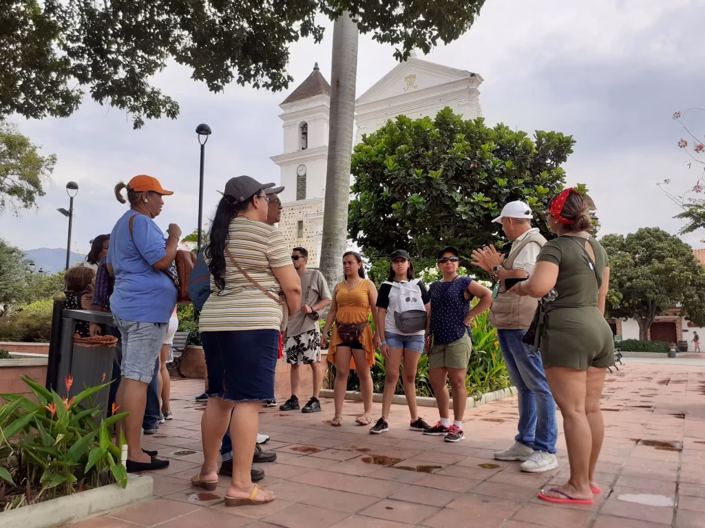 Travelers listening to their guide on the Plaza Mayor of Santa Fe de Antioquia, with the cathedral tower behind