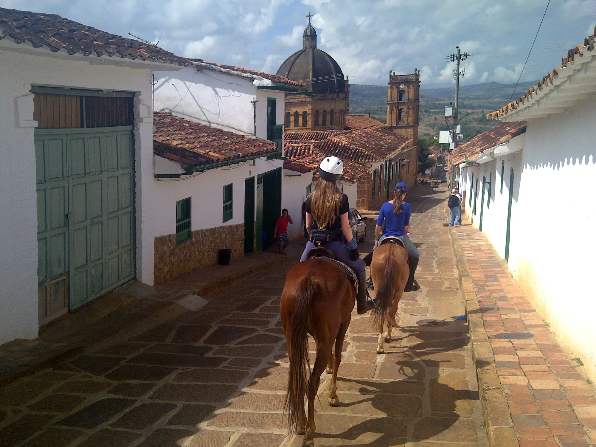 Horseback riders passing whitewashed houses and a historic church in the heart of Barichara Tour scenery.