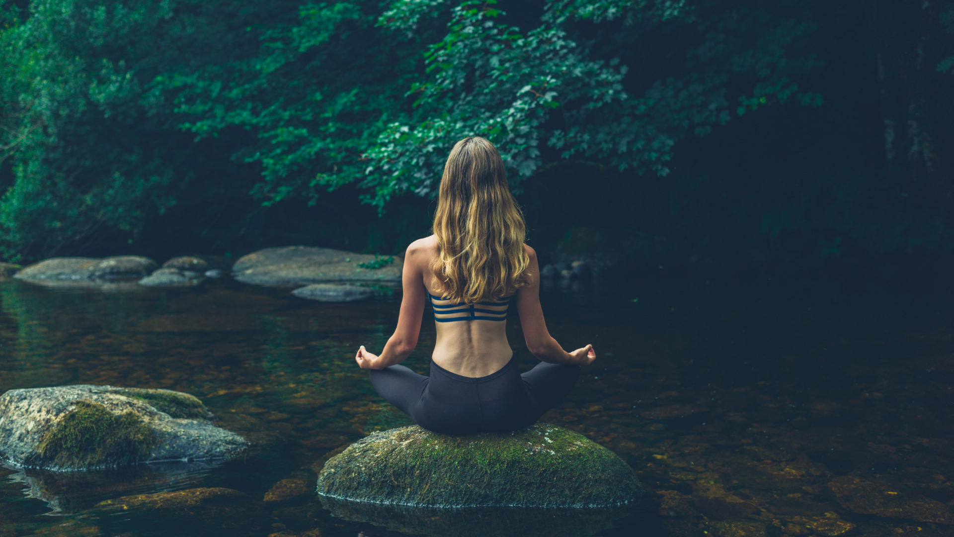 Traveler meditating on a rock surrounded by calm water and jungle at the Natural pool Palomino.