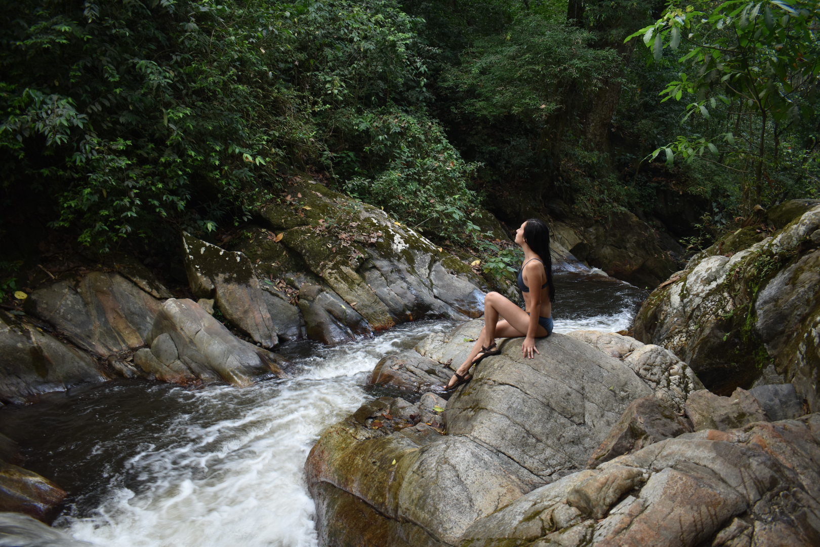 Woman sitting on a riverside rock surrounded by tropical forest on a Minca Tour Santa Marta adventure.