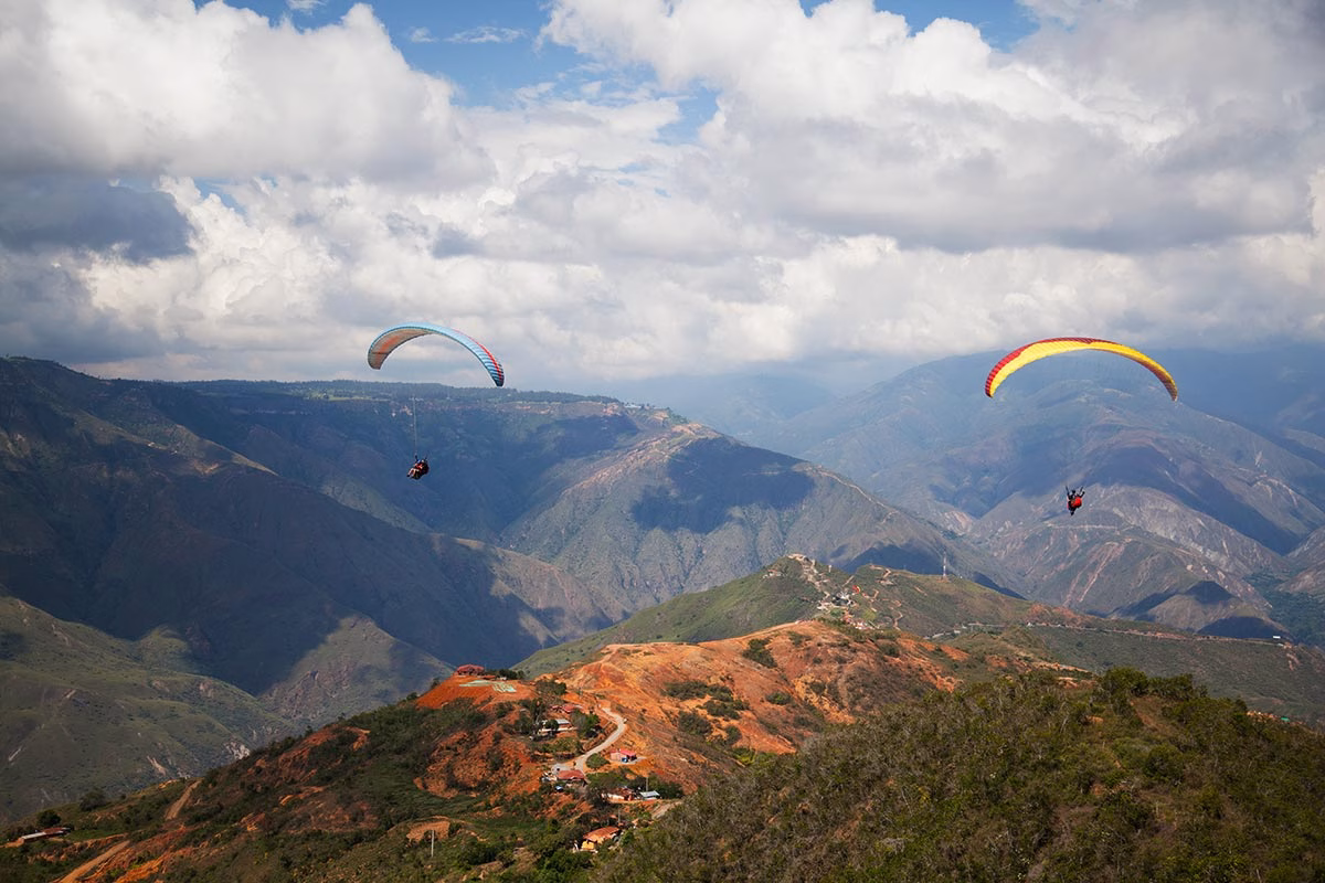 Two paragliders gliding over the vast mountains and rugged landscape of paragliding Chicamocha Canyon.