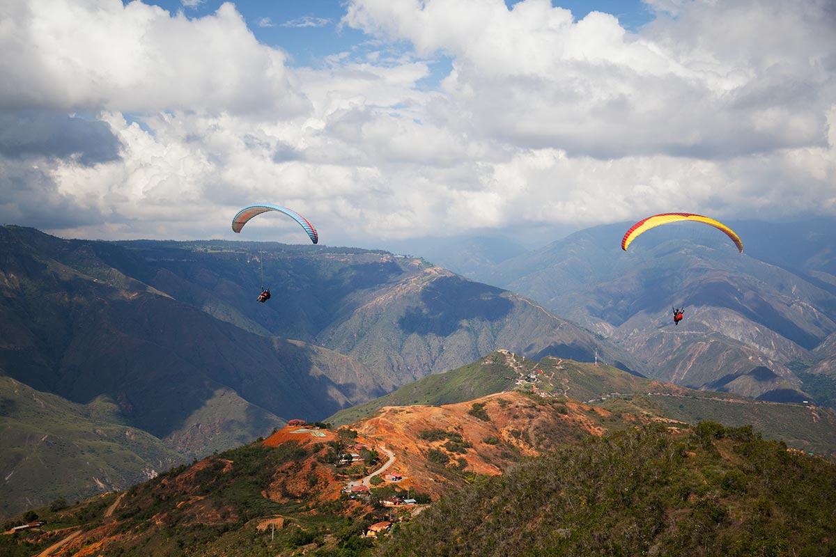 Two paragliders gliding over the vast mountains and rugged landscape of paragliding Chicamocha Canyon.