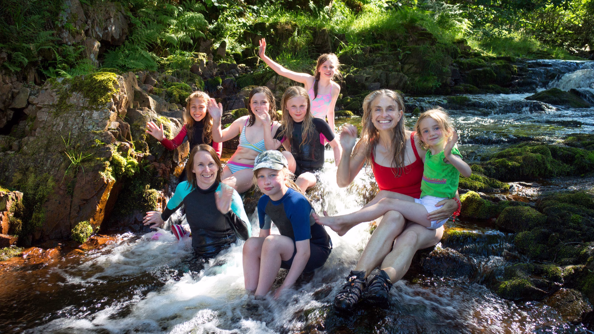 Familia sentada en una quebrada poco profunda y sonriendo durante una visita a la piscina natural de Palomino.