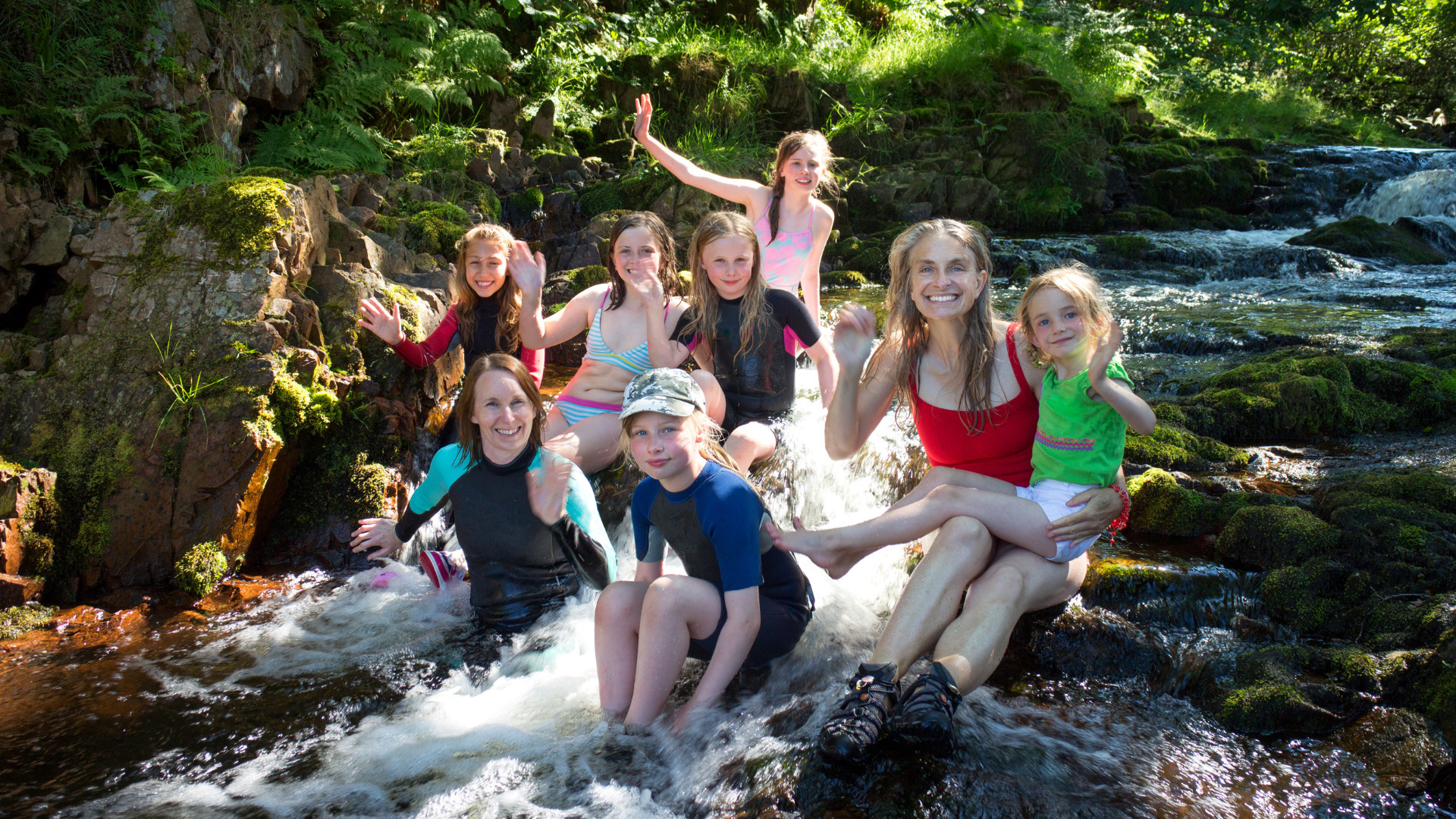 Family sitting in a shallow stream and smiling during a visit to the Natural pool Palomino.