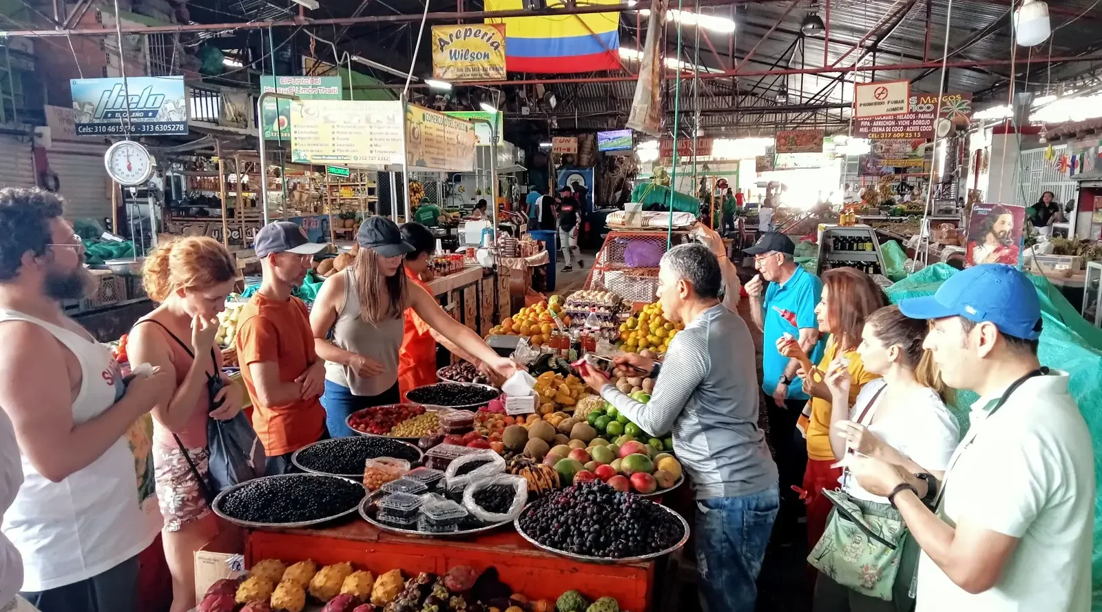 Travelers tasting tropical fruits at a busy local market during a Food Tour Cali experience in Colombia.