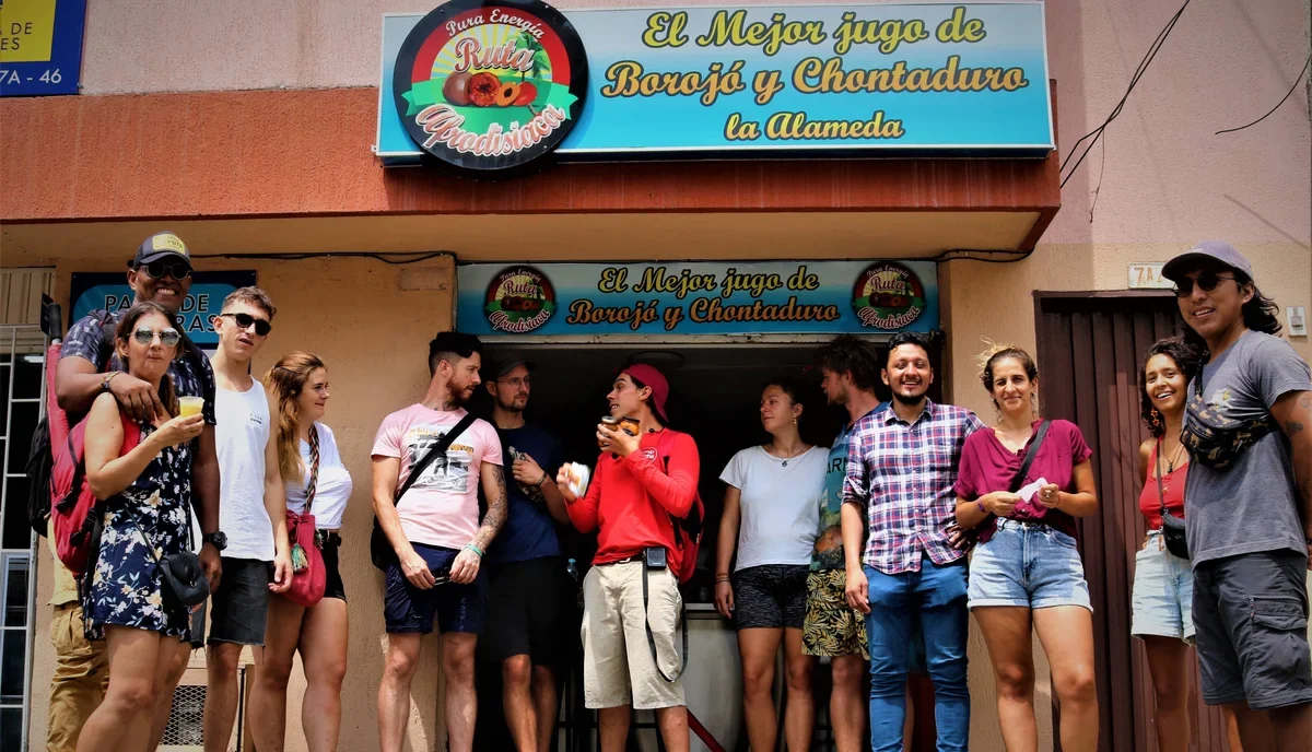 Travelers stopping for traditional borojó and chontaduro juice at a local market stand during a Food Tour Cali.