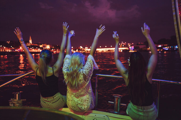 Three women enjoying the illuminated bay at night during a Cartagena sunset boat tour private, with city lights glowing in the background.