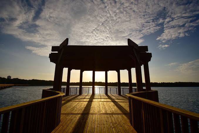 Sunrise view from a wooden pavilion over the lagoon at Mallorquin Eco-Park, with dramatic clouds and reflections across the water.