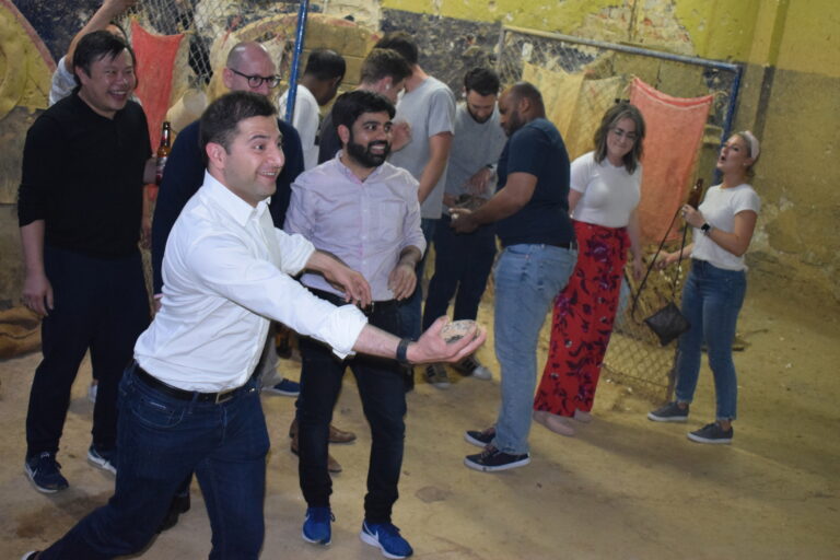 A player about to throw at a tejo court in Medellín while the group watches with beers