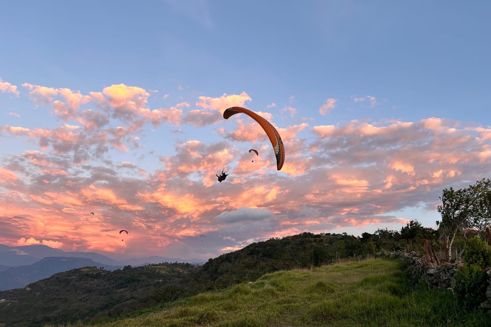Paraglider flying across a colorful sunset sky during a scenic paragliding Chicamocha Canyon tour.